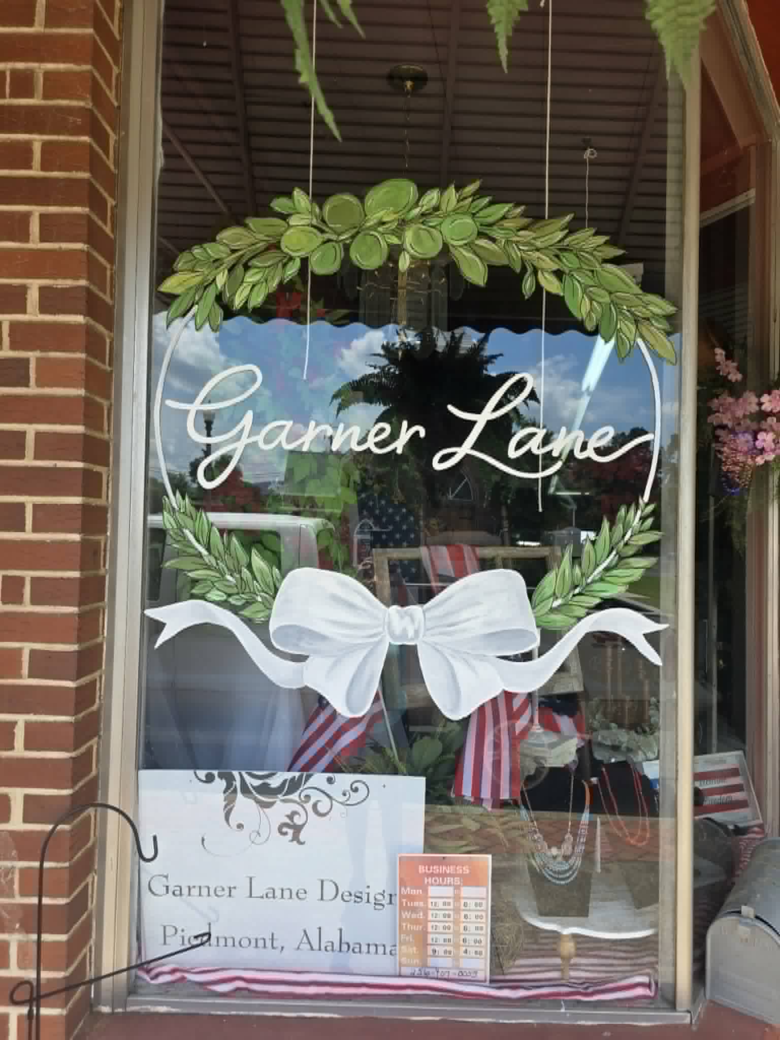 Garner Lane Designs storefront window painted with white script lettering inside a green laurel wreath topped with a hand-tied white bow