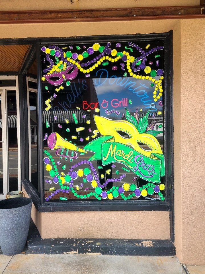 Mardi Gras window painting with masks, beads, and trumpet at Bar & Grill