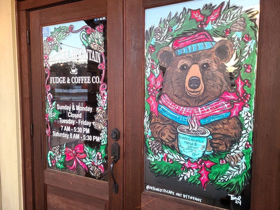 Christmas window painting of a bear in a hat and scarf holding coffee at Dugger Mountain Fudge & Coffee Co.