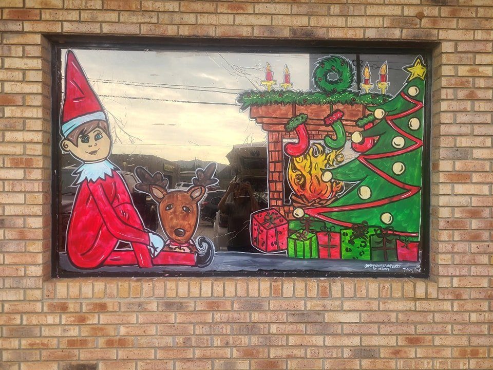 Christmas window painting of Elf on the Shelf with reindeer beside a fireplace and Christmas tree