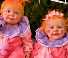 Two toddlers in pastel clown costumes with rosy painted cheeks