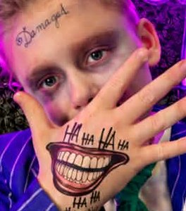 Boy with Joker-inspired Halloween makeup and a painted smile on his hand