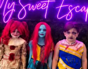 Three kids in character costumes with full face makeup under the My Sweet Escape neon sign